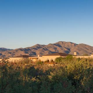 A serene desert landscape with mountains in the background and a building nestled among the vegetation at sunset.