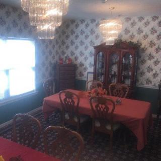 A classic dining room featuring a large dining table with a red tablecloth, elegant chandeliers, and a wooden cabinet against patterned wallpaper.