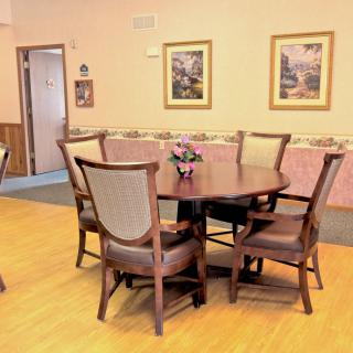 A cozy dining room with a round table and six chairs, adorned with paintings on the walls.