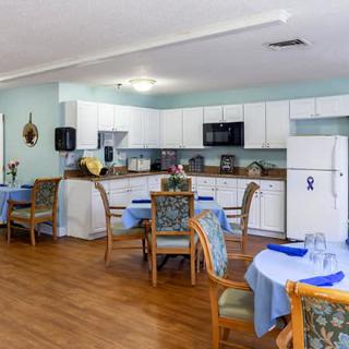 A cozy dining area with round tables set for meals, adjacent to a kitchen with white cabinets.