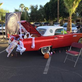 A classic red car decorated for Halloween with cobwebs and a pumpkin in a parking lot.