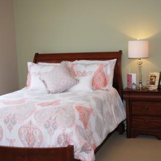 A cozy bedroom with a neatly made bed, featuring patterned bedding, a wooden nightstand, and a lamp.