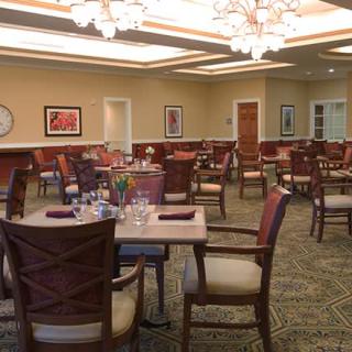 A well-lit dining room with neatly arranged tables and chairs, featuring elegant chandeliers.