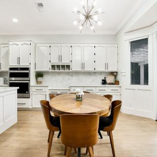 A modern kitchen with white cabinets, a round wooden dining table, and stylish lighting.