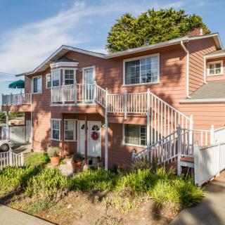 A charming two-story house with a front garden and balcony, featuring exterior stairs.