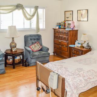A cozy bedroom with a hospital bed, two blue armchairs, and a wooden dresser.
