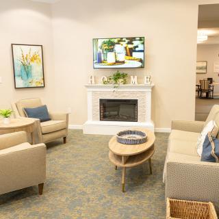 A cozy living room with modern furniture, including sofas and armchairs arranged around a coffee table in front of a fireplace and television.