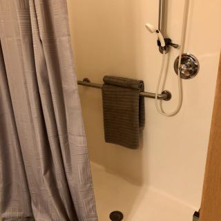 A bathroom shower with a curtain, handrail, and towel hanging.
