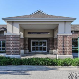 A brick building entrance with columns and a landscaped area in front.