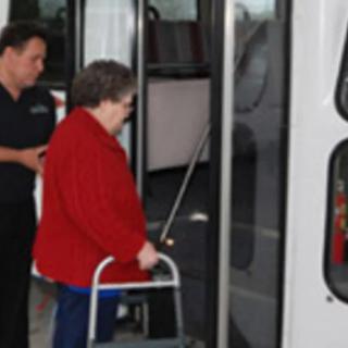 An elderly woman using a walker is being assisted while boarding a bus.