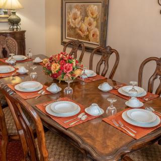 A beautifully set dining table with elegant dinnerware, a floral centerpiece, and warm interior lighting.