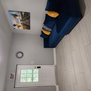 A minimalist living room with a blue sofa, accented with yellow cushions, a wall clock, and artwork above the couch.