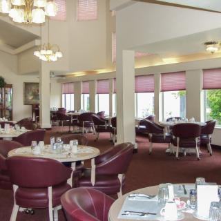 An empty dining room with tables and chairs arranged neatly, featuring large windows and elegant chandeliers.