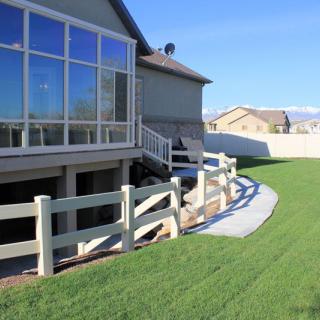 A suburban backyard with a green lawn, fenced area, and a patio.