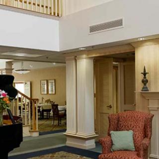 A cozy lobby interior with an armchair, piano, and floral arrangement.