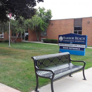 A view of the exterior of a community building featuring a bench and a sign.