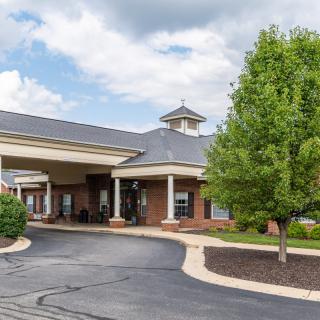 A brick building with a covered entrance and surrounding greenery under a cloudy sky.