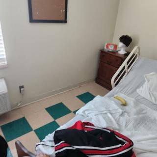 A room featuring a medical bed, some personal items, and an unmade bed with a banana on it.