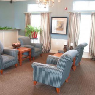 A cozy living room with blue upholstered chairs and a table, decorated with plants and a painting on the wall.