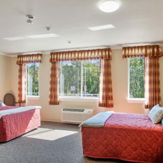 A spacious hotel room with two beds, large windows, and ample natural light.