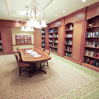 A cozy library room with wooden bookshelves, a central table, and warm lighting.