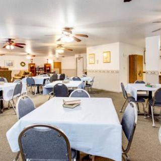 A spacious dining area with multiple tables and chairs, featuring ceiling fans and a simple decor.