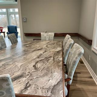 A spacious dining room with a large marble-patterned table and cushioned chairs, illuminated by natural light from a window.