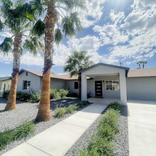 A charming modern home surrounded by palm trees and a well-maintained landscape under a beautiful cloudy sky.