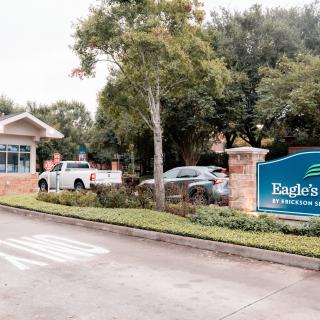 Entrance of a residential community with vehicles and lush greenery.