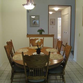 A cozy dining room with a wooden table and chairs, decorated with a small plant and soft lighting.
