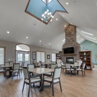 A spacious dining area with modern decor, featuring a high ceiling, chandelier, and cozy fireplace.