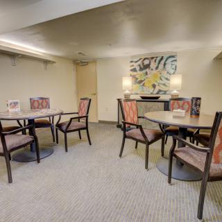 A cozy dining area with tables and chairs, adorned with artwork and carpet flooring.