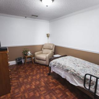 A simple room featuring a single bed, an armchair, and basic furnishings.