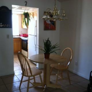 A small dining area with a round table and two chairs, adjacent to a kitchen with natural light coming in.