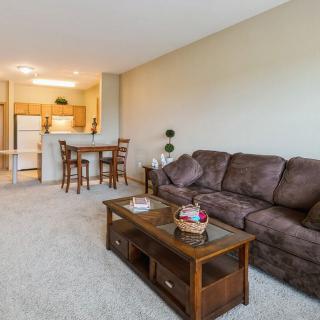 A cozy living room with a brown sofa, wooden coffee table, and a view into the kitchen and dining area.