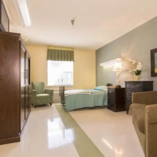 A clean and neatly arranged hospital room with a single bed, armchair, and window.