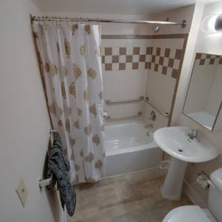 A compact bathroom featuring a bathtub with a shower curtain, a pedestal sink, and a mirror above it.