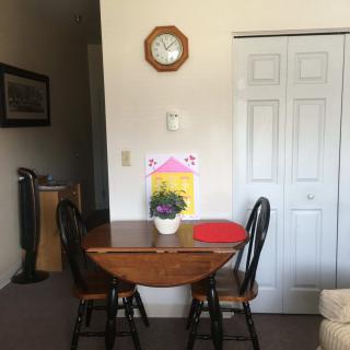 A cozy dining area with a small wooden table, two chairs, a wall clock, and a potted plant.