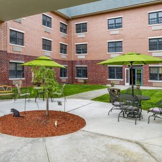 A tranquil courtyard with outdoor seating and green umbrellas next to a brick building.
