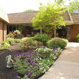 A beautifully landscaped garden with vibrant flowers and a tree near a building entrance.