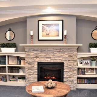A stylish and modern living room featuring a stone fireplace, neatly arranged shelves, and elegant decor.