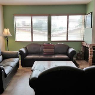 A cozy living room with two sofas, a coffee table, and a fireplace, illuminated by natural light from the windows.