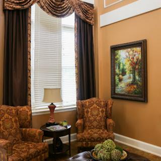 A cozy living room corner featuring elegant curtains, patterned armchairs, and a beautiful painting.