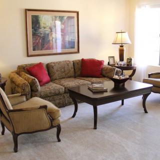 A cozy living room featuring a patterned sofa with red throw pillows, a matching armchair, and a dark wood coffee table. A lamp and wall art enhance the inviting atmosphere.