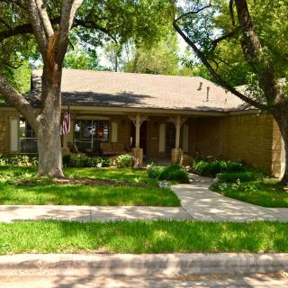 A charming suburban house with a neatly manicured lawn and mature trees.