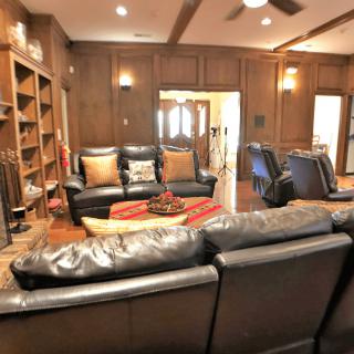 A cozy living room with leather sofas and wood-paneled walls featuring bookshelves.
