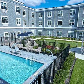 A modern apartment complex features a fenced swimming pool and well-maintained outdoor area under a clear blue sky.