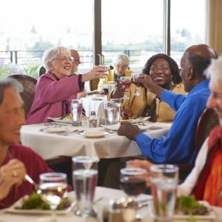 A group of elderly friends enjoying a meal together, raising their glasses in celebration at a restaurant.