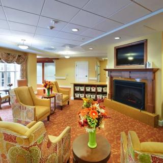 A cozy living room with comfortable seating arranged around a fireplace and television, decorated with floral arrangements and warm lighting.