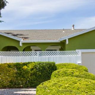 A green house with a white fence and neatly trimmed bushes in front.